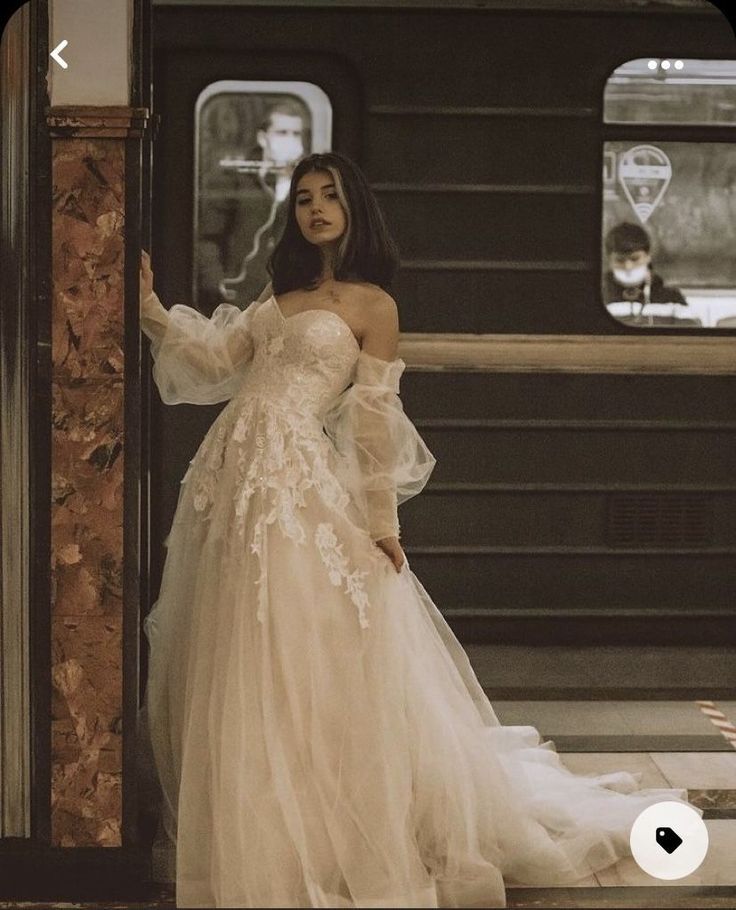 a woman in a wedding dress standing next to a train platform with her hand on the rail