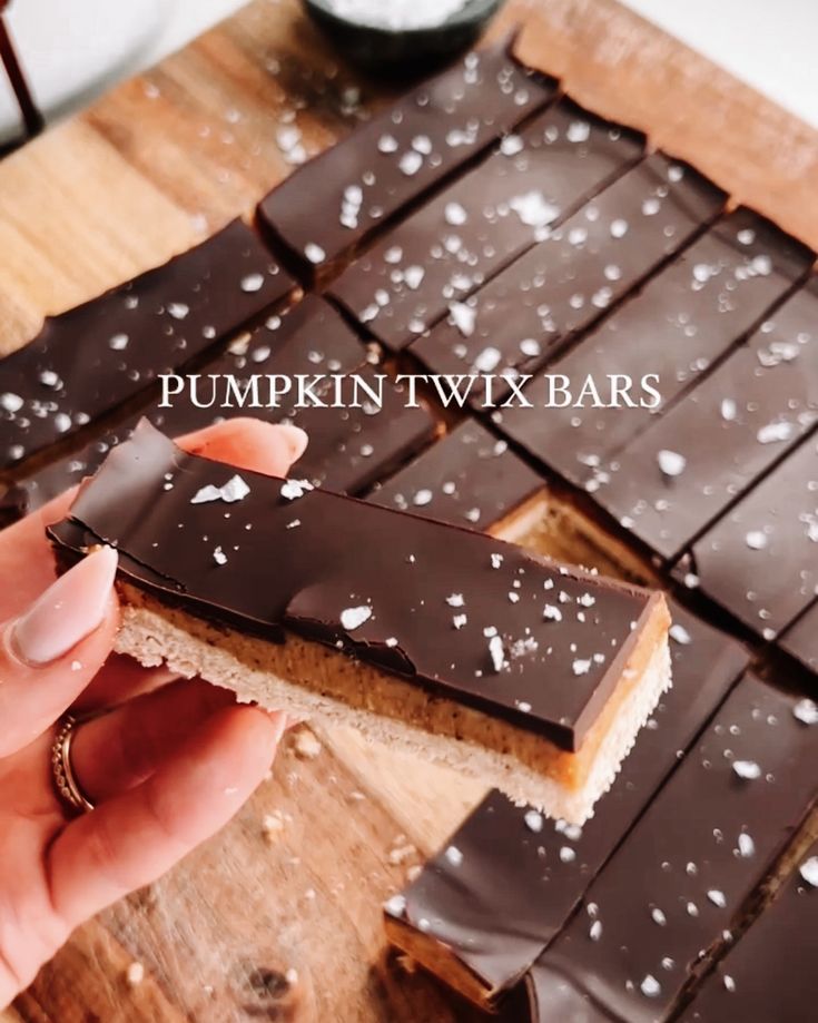 a person holding a piece of chocolate bar on top of a wooden cutting board