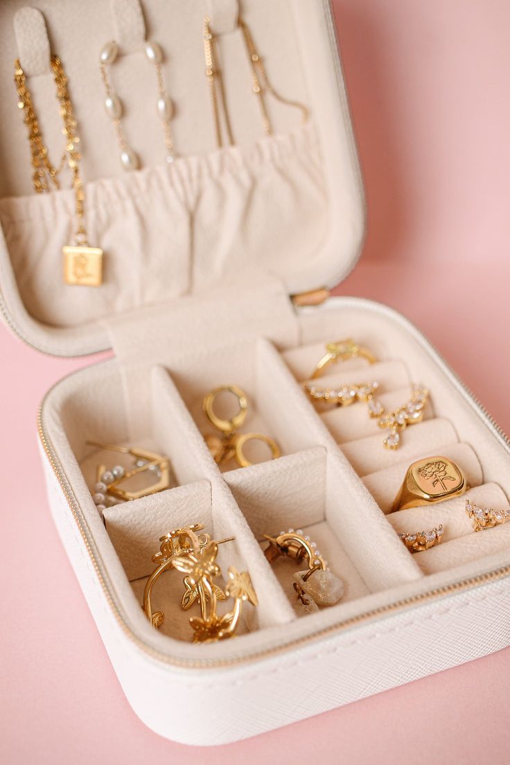 an open jewelry box filled with lots of different types of rings and bracelets on top of a pink surface