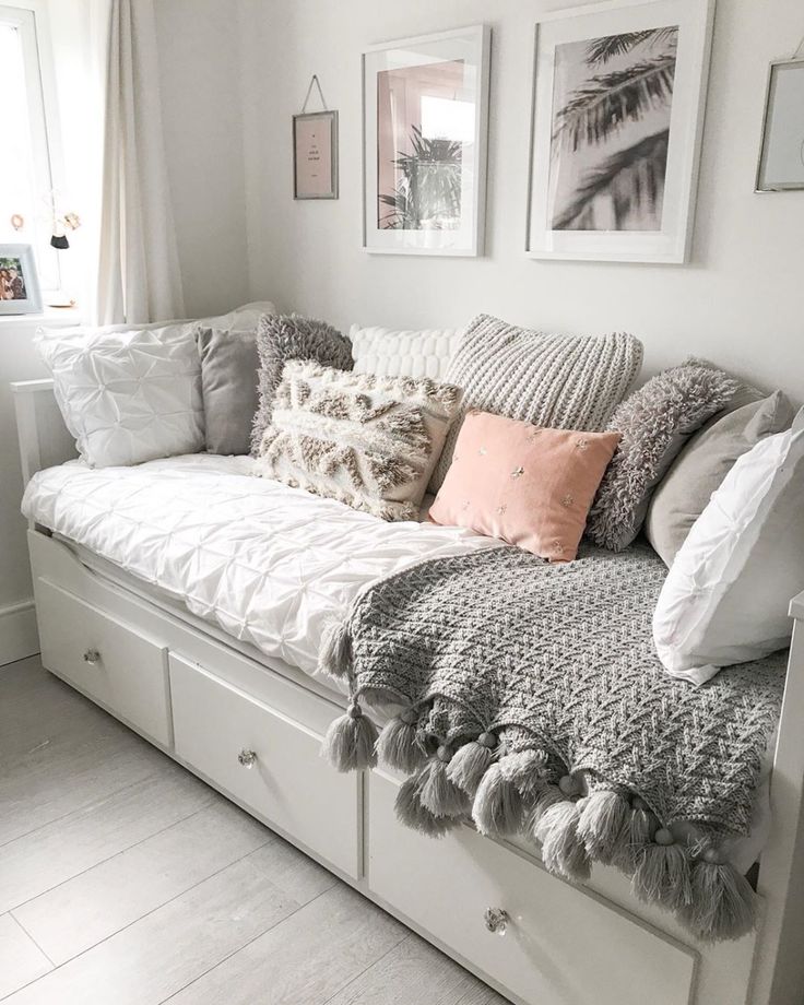 a white couch with lots of pillows and blankets on it's back, sitting in front of a window