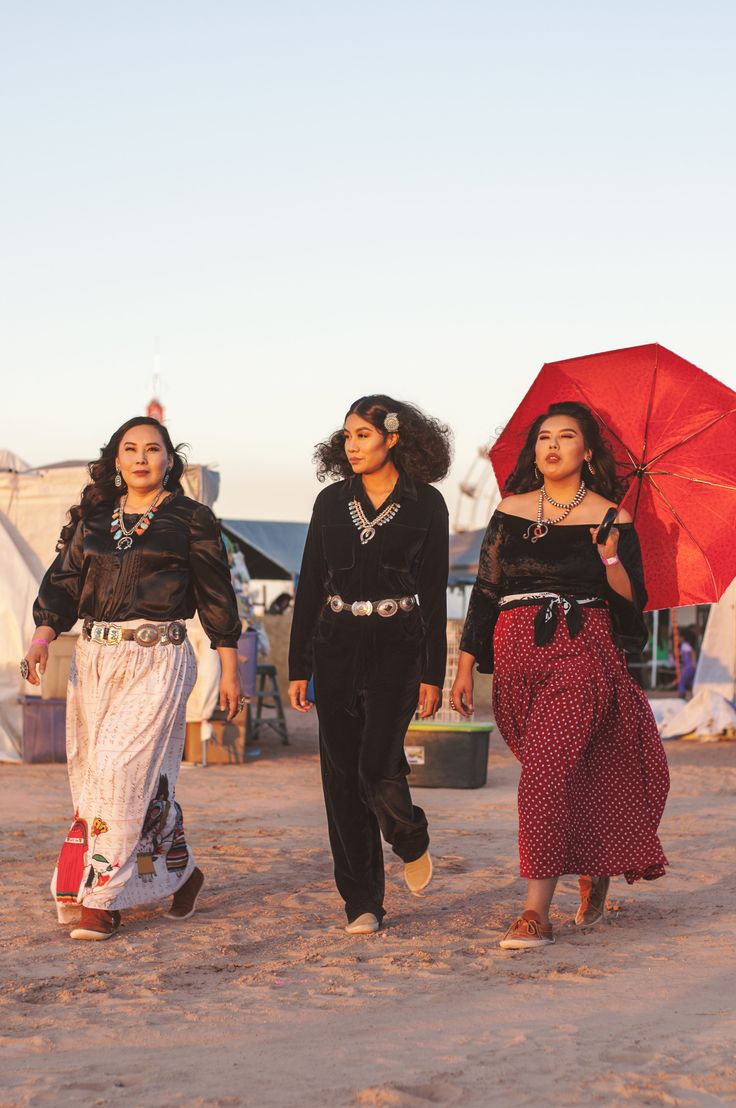 three women walking in the sand with an umbrella