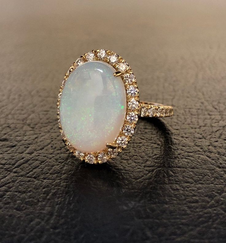 DeKara Designs Collection Our latest design! An Elegant Art Deco Inspired Australian Opal Surrounded by Beautiful Round Diamonds in an Halo 14K Yellow Gold Setting. Metal- 14K Yellow Gold, .583. The Opal is a fully cabochon cut Australian Opal. Not lab created, not a doublet, or a triplet. Stones- Center Features an Oval Fiery Australian Opal 5.80-6.00 Carats 15.60 MM Long, 11.50 MM Wide, 34 Round Diamonds, F-G Color VS1 Clarity, 0.92 Carats. The opal will be matched as close as possible to the Heirloom Oval Opal Ring For Formal Occasions, Luxury Oval Wedding Ring, Luxury Oval Opal Ring For Anniversary, Exquisite Oval Opal Ring, Luxury Oval Ring Jewelry For Wedding, Luxury Oval Jewelry For Anniversary, Luxury Oval Jewelry For Wedding, Elegant 14k Gold Oval Opal Ring, Elegant Oval Opal Ring In 14k Gold