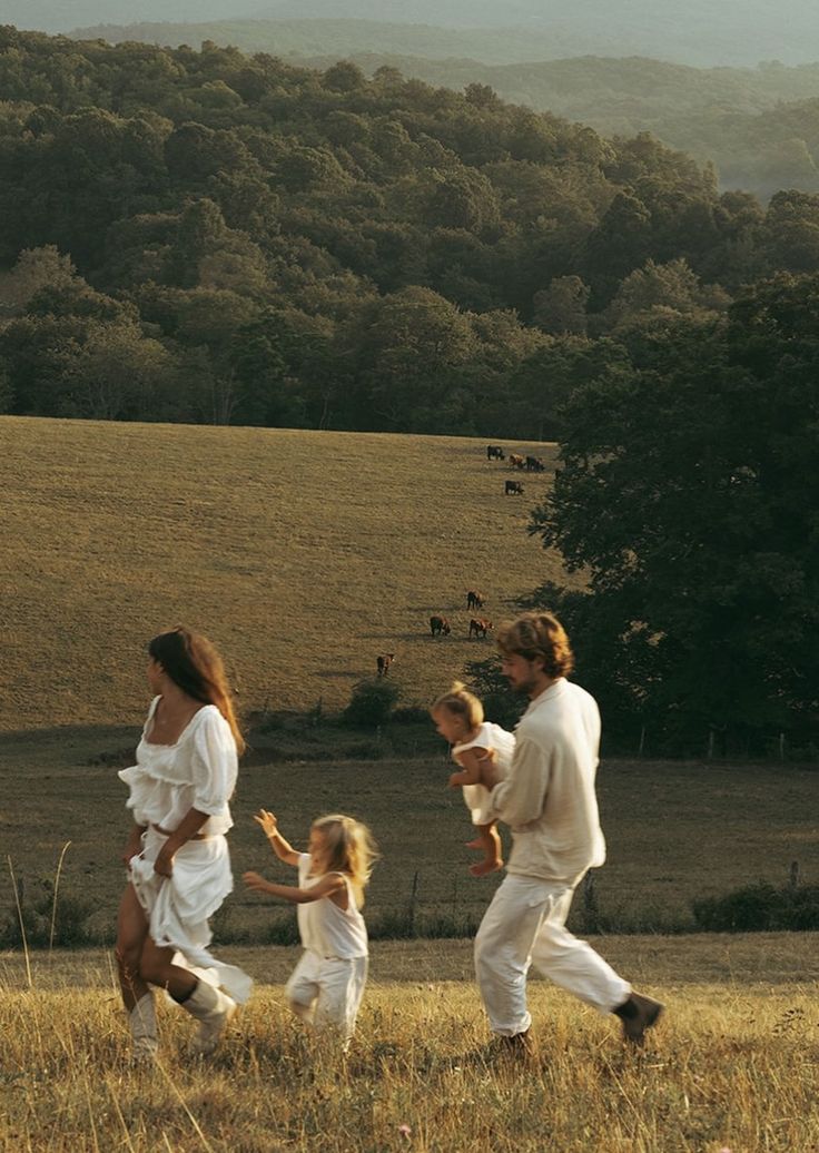 a man and two women are walking with their children in a field near some trees