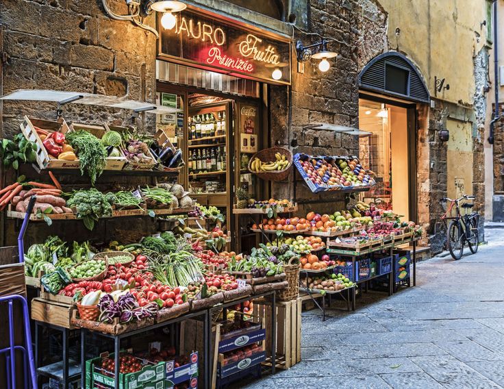 an outdoor market with fruits and vegetables on display in front of the storefronts