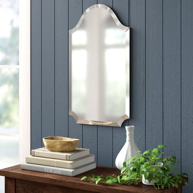 a mirror on the wall above a table with books and a vase next to it