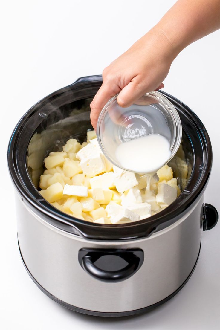 someone is pouring milk into a crock pot filled with diced potatoes and tofu