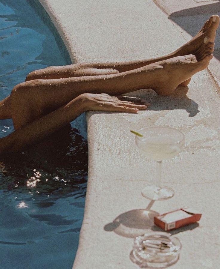 a woman laying on the side of a swimming pool next to a glass of wine