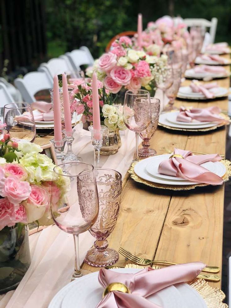 the table is set with pink and white flowers, gold place settings, and silverware