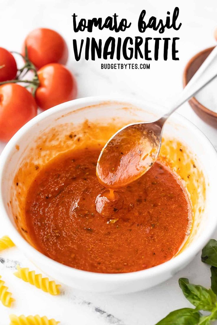 a bowl of tomato basil vinagrete sauce with a spoon in it and some tomatoes on the side