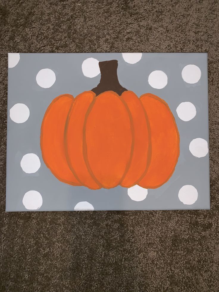 an orange pumpkin painted on a gray and white polka doted paper with dots around it