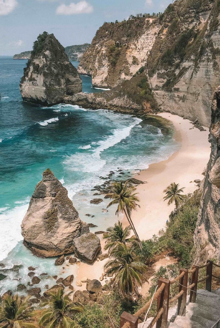 stairs lead down to the beach with palm trees on either side and blue water in the background