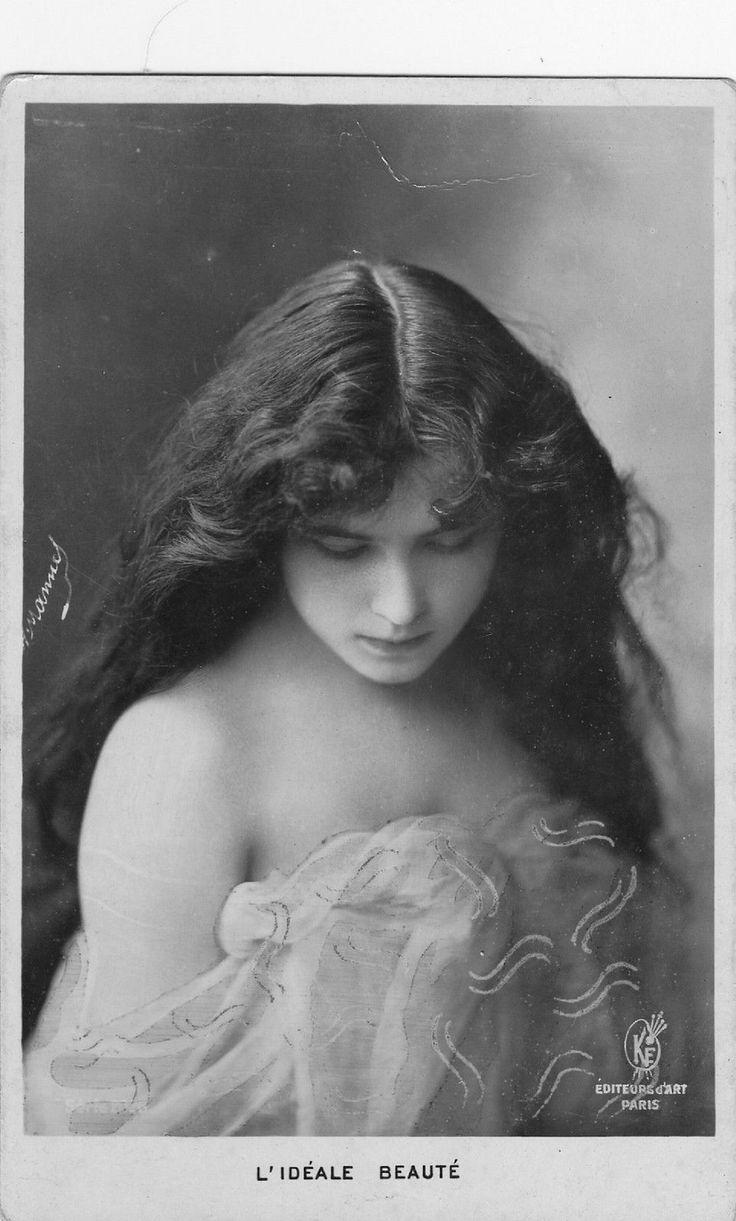 an old photo of a young woman with long brown hair and blue dress looking down