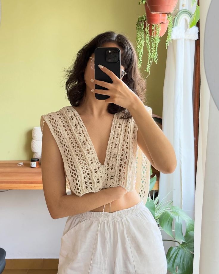 a woman taking a selfie in front of a mirror wearing white shorts and a crochet top