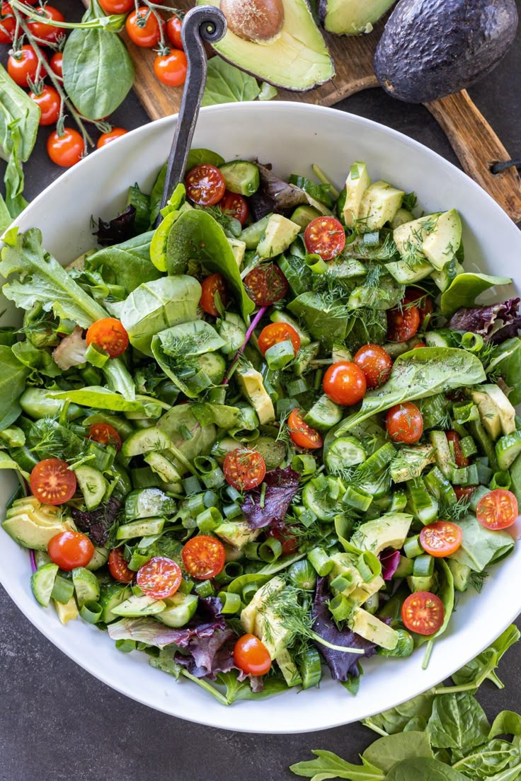 a salad with avocado, cherry tomatoes and spinach in a white bowl