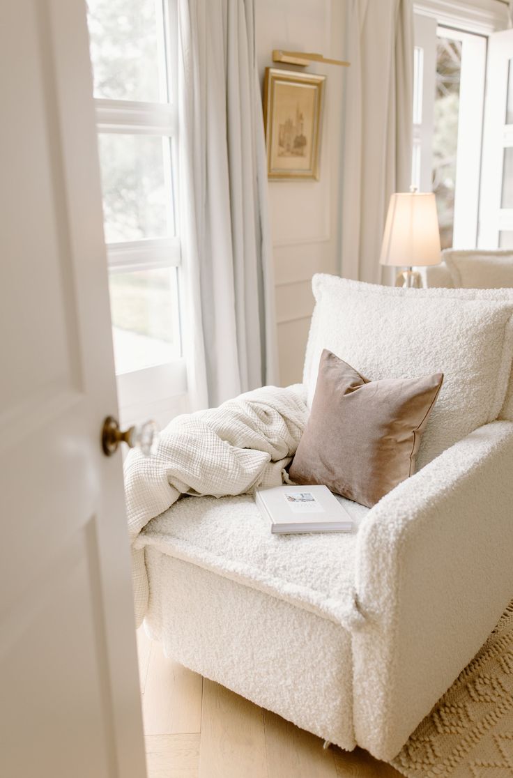 a white chair sitting in front of a window next to a lamp and a door