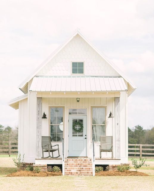 a small white house with two chairs on the front porch