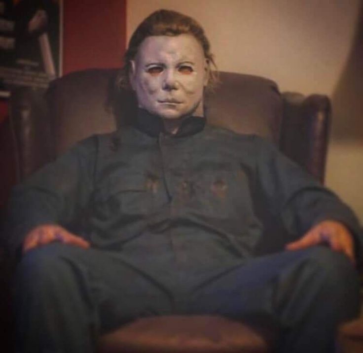 a man sitting in a chair with his hands on his hips wearing a creepy mask