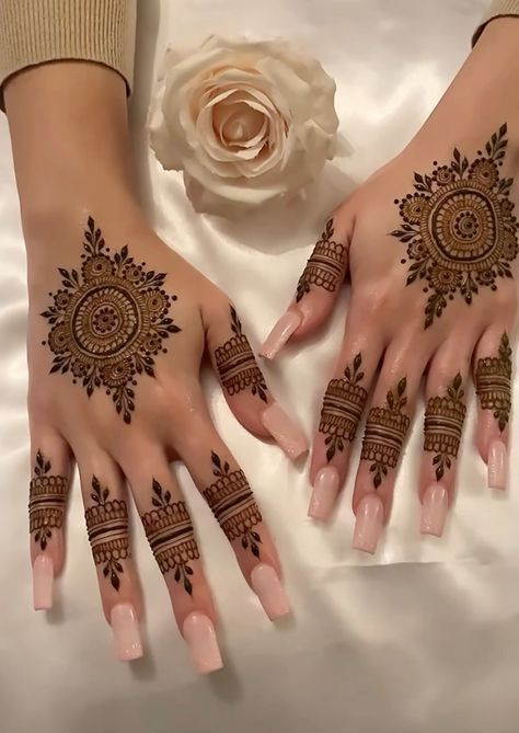 two hands with henna tattoos on them next to a white rose and a flower