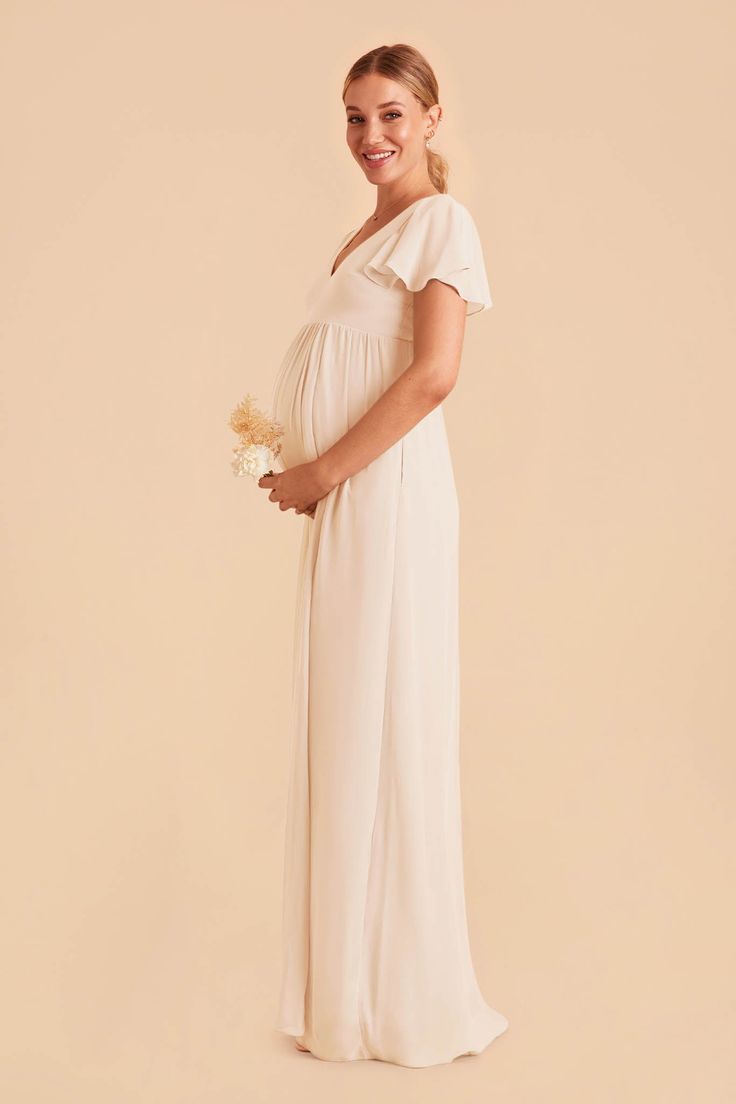 a pregnant woman wearing a white gown and holding a flower in her hand, posing for the camera