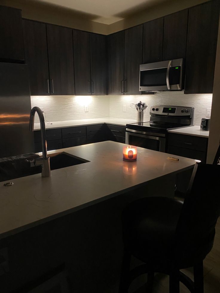 a lit candle is sitting on the counter in a kitchen with dark wood cabinets and stainless steel appliances