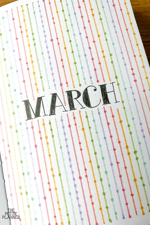 a card with the word march written in black ink on it and rainbow colored stripes