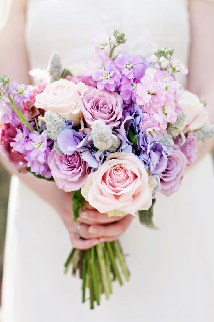 a bride holding a bouquet of purple and pink flowers on her wedding day at the park