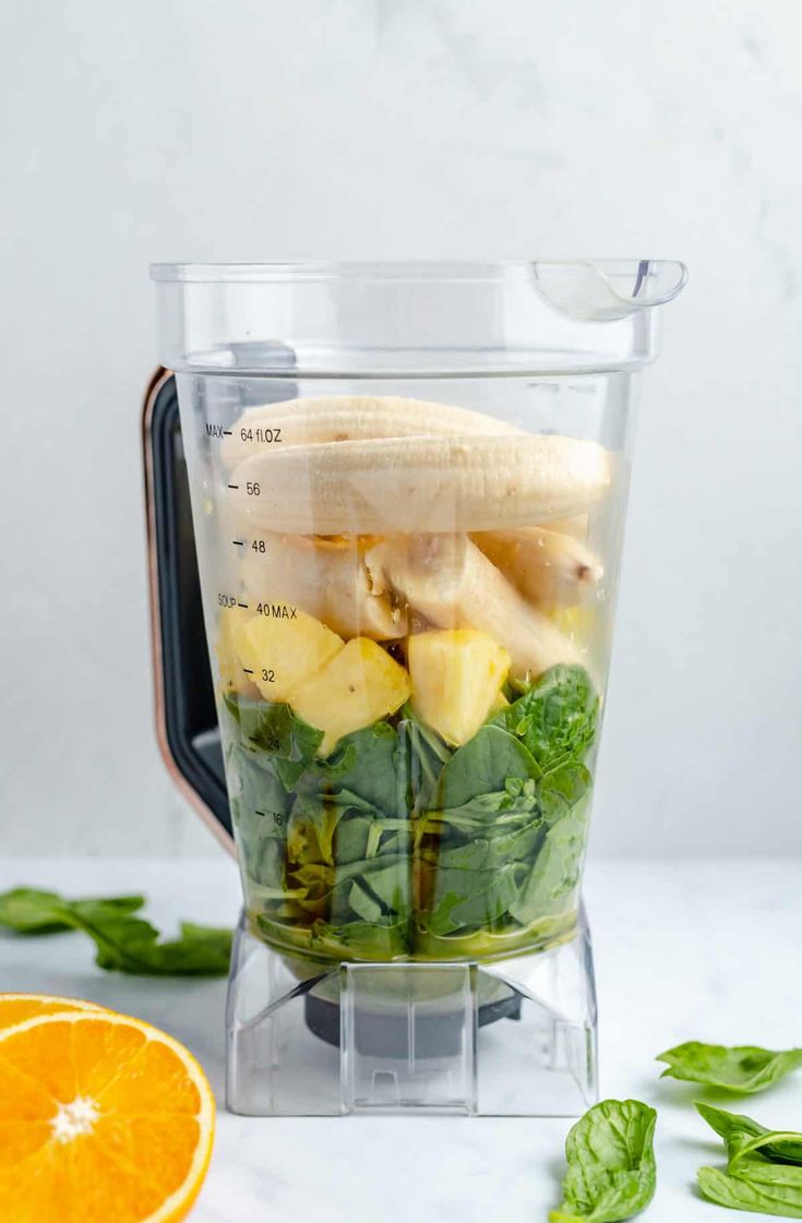 a blender filled with fruit and vegetables on top of a counter next to an orange slice