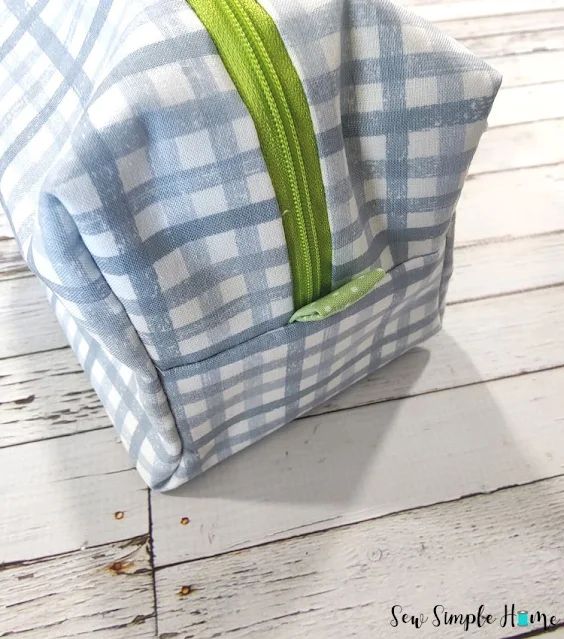 a blue and white checkered bag sitting on top of a wooden floor next to a green zipper