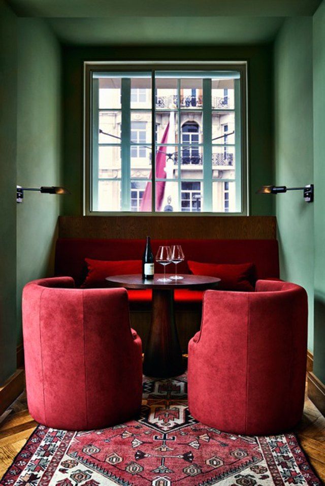 two red chairs sitting on top of a rug next to a table with wine glasses