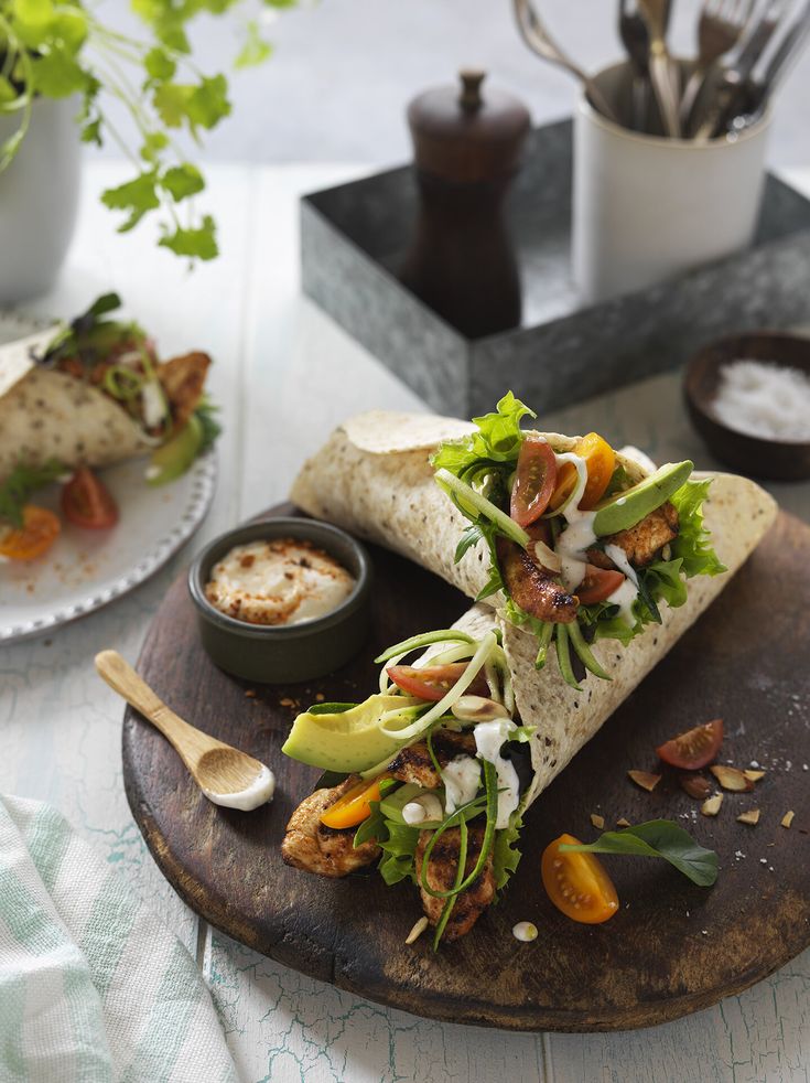 a burrito with lettuce, tomatoes and other toppings on a wooden plate