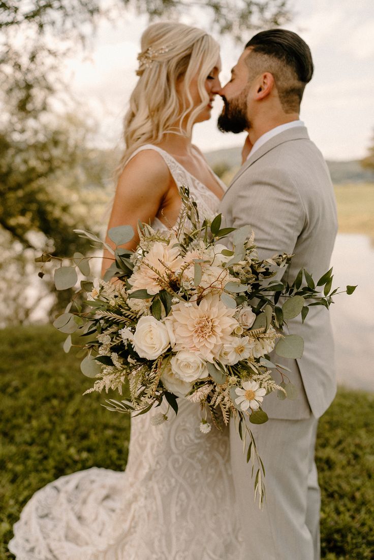 a bride and groom standing next to each other in front of a lake with greenery