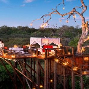 a tree house with lights on the roof and some people sitting in it at night