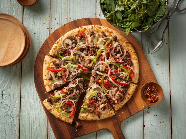 a pizza sitting on top of a wooden cutting board next to a bowl of greens