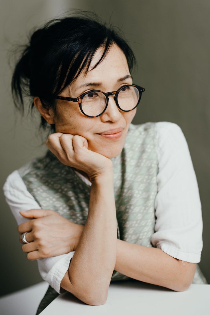 a woman wearing glasses sitting at a table with her hand on her chin and looking to the side