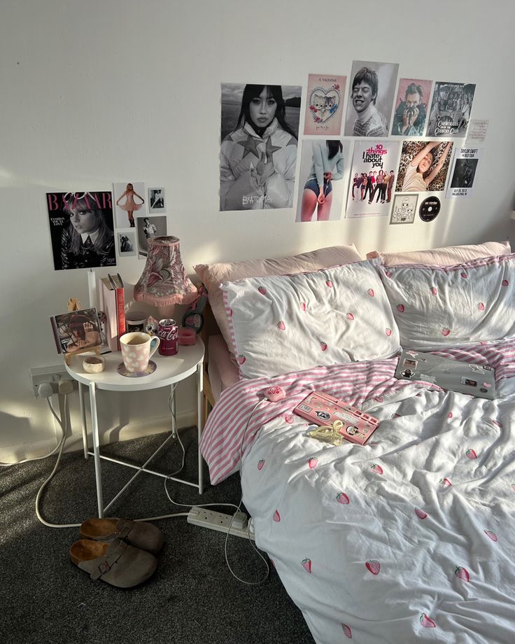 a bedroom with pink and white bedding, pictures on the wall and a small table