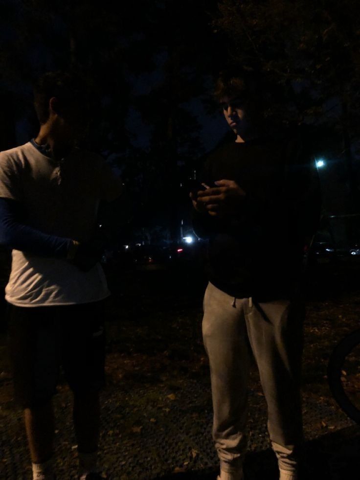 two people standing next to each other in the dark with their cell phones up against their backs