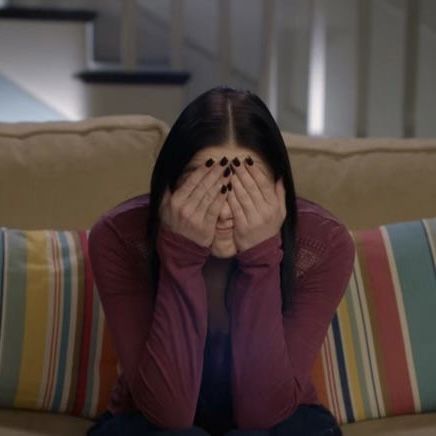 a woman covering her eyes while sitting on a couch in front of a striped pillow