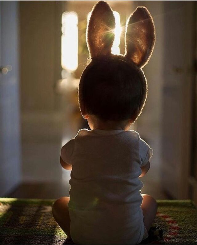 a little boy that is sitting down with a bunny ears on his head and back