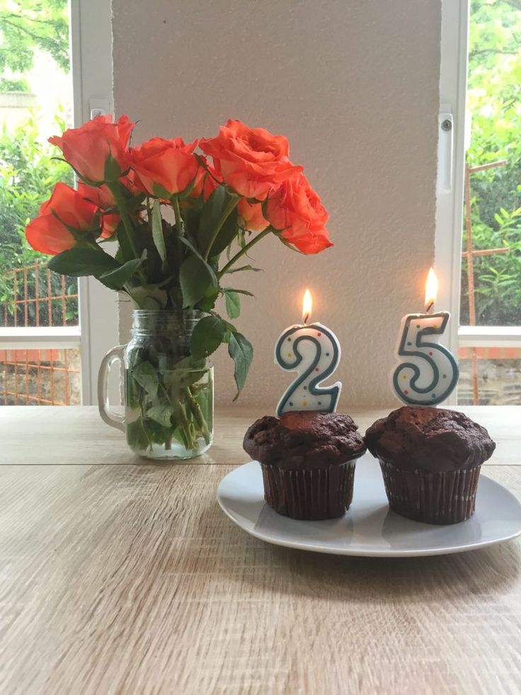 two cupcakes on a plate with candles and flowers in front of the cake