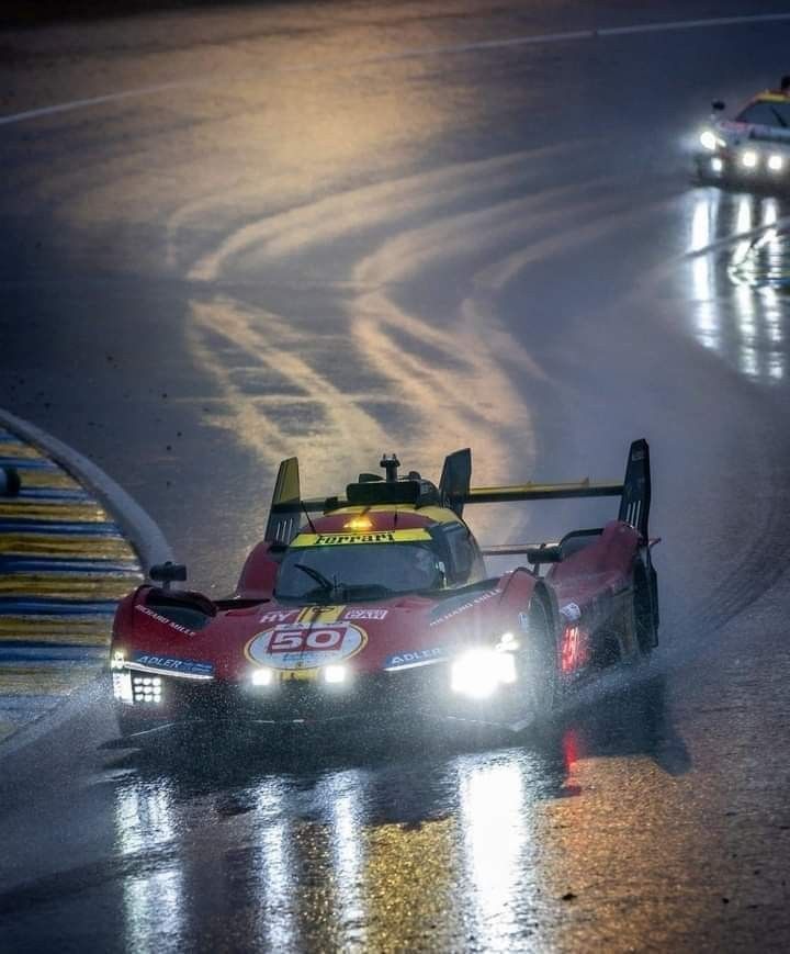 two race cars driving on a wet track at night with fog coming from behind them