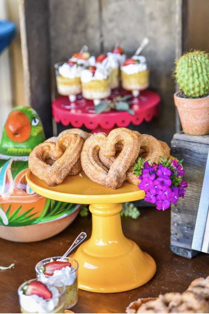 an assortment of desserts and pastries displayed on a table with cactus in the background