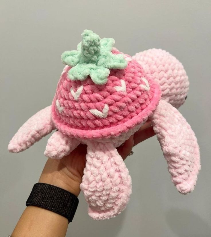 a hand holding a pink crocheted stuffed animal with a green leaf on top