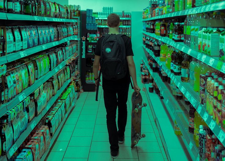 a man with a skateboard walks down the aisle of a grocery store