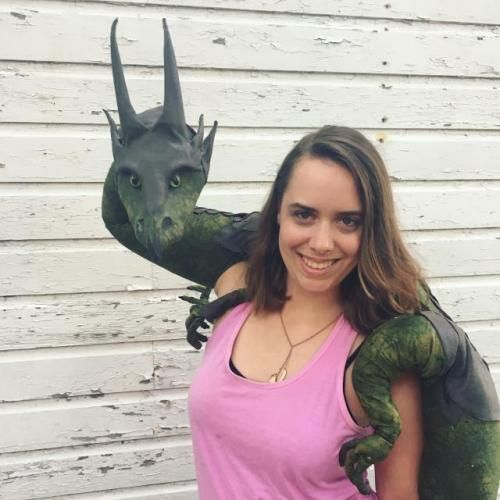 a woman in pink shirt standing next to a green dragon statue with large horns on it's head