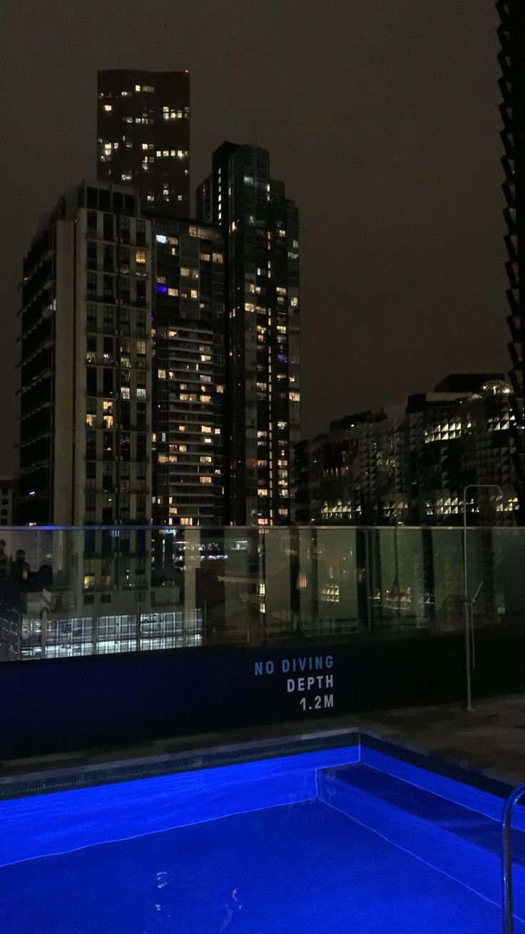 an empty swimming pool in the middle of a city with skyscrapers lit up at night