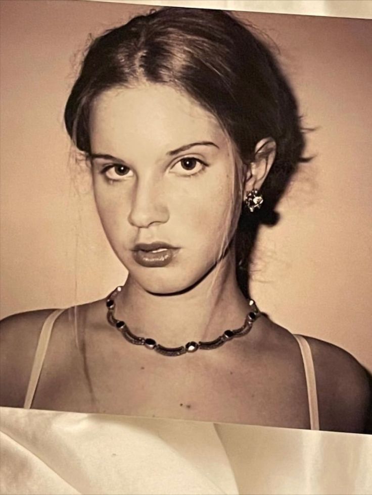 a black and white photo of a young woman wearing a necklace with pearls on it