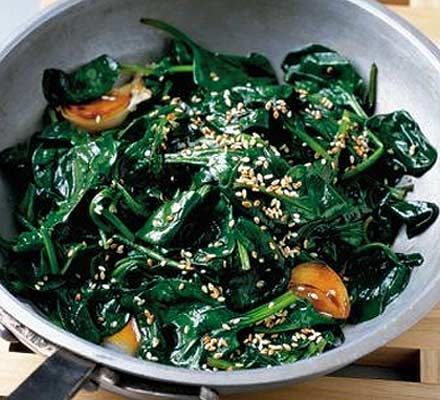 spinach stir fry with sesame seeds and seasoning in a pan on a wooden table