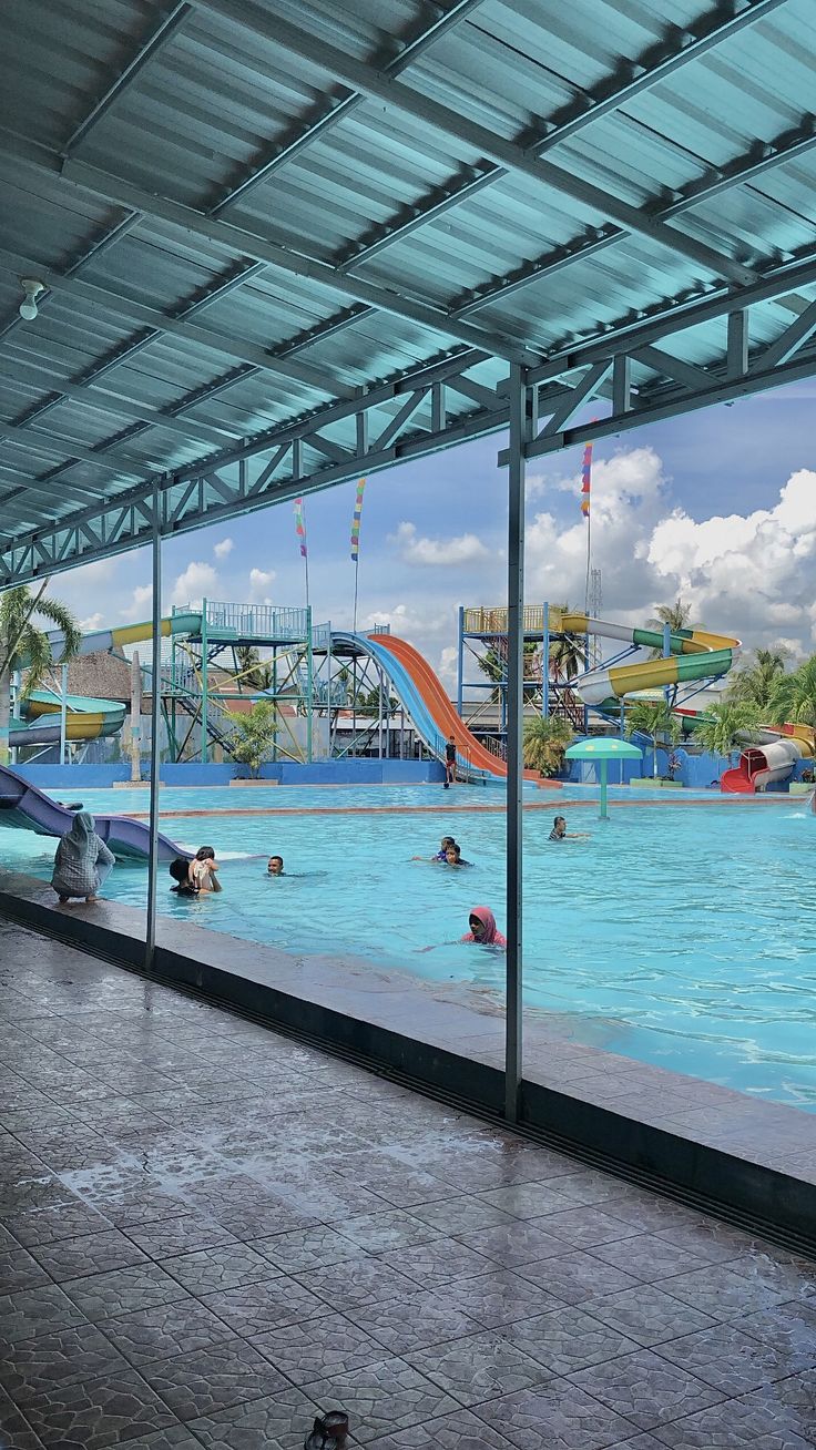 an indoor swimming pool with people in it and water slides behind the glass wall that overlooks them