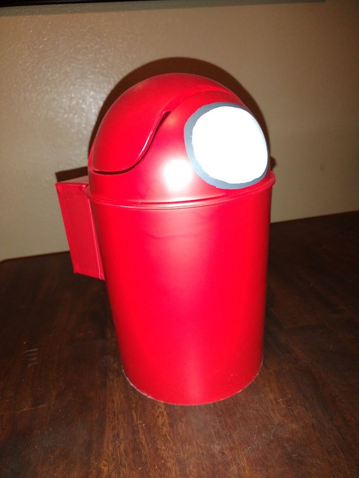 a red trash can sitting on top of a wooden table next to a white light