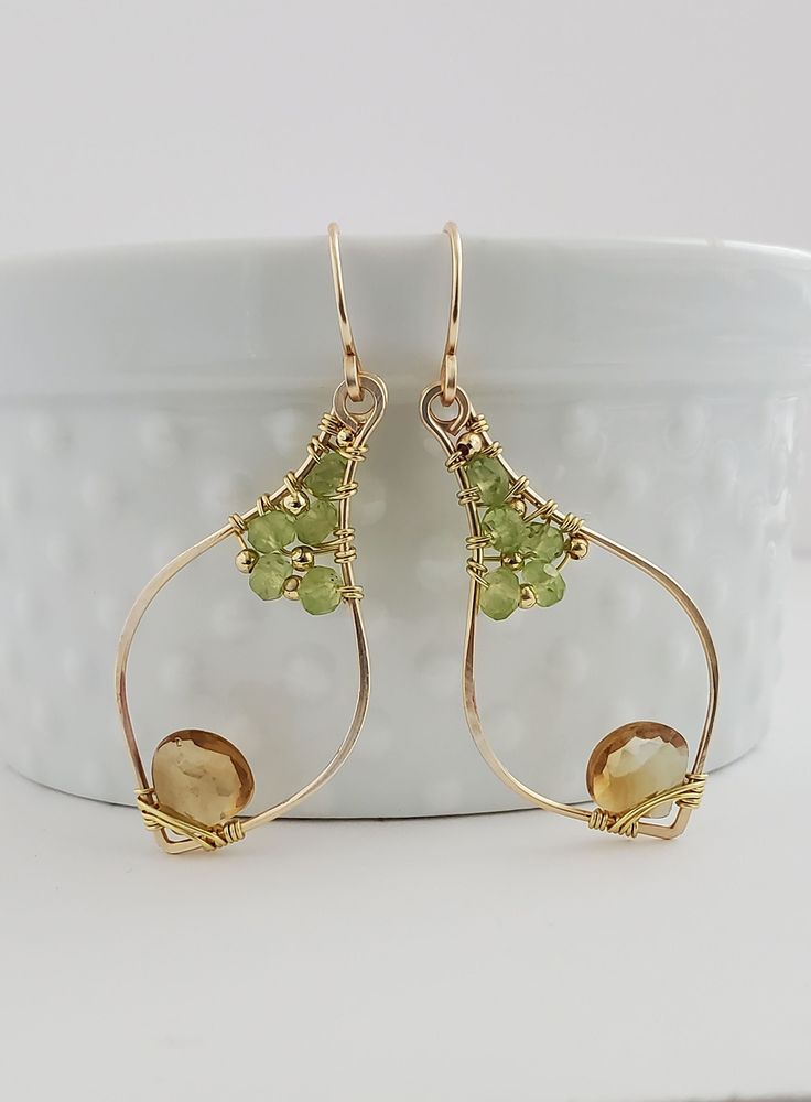 "JANUS Citrine and Peridot Gold Filled Earrings Named after the Roman God JANUS, these boho chic earrings represent change and transitions with its two color design, symbolizing the changing of colors from summer to autumn. Handmade from:  - Citrine heart  - Peridot beads  - 14K Gold Filled metal and beads Citrine & Peridot: The energy of this combination produces luck and confidence.  Peridot is connected with prosperity and abundance, and Citrine is associated with positivity and joy.  Togethe Cheap Handmade Gold Wrap Earrings, Peridot Dangle Earrings With Ear Wire, Gold Peridot Gemstone Earrings, Peridot Dangle Earrings In Gold, Gold Peridot Earrings For May Birthstone, Yellow Gold Peridot Dangle Earrings, Gold Teardrop Peridot Earrings, Two Color Design, Autumn Handmade